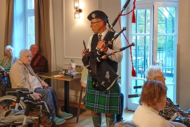 Dudelsackspieler in Kilt spielt vor älteren Zuhörern in einem Saal.